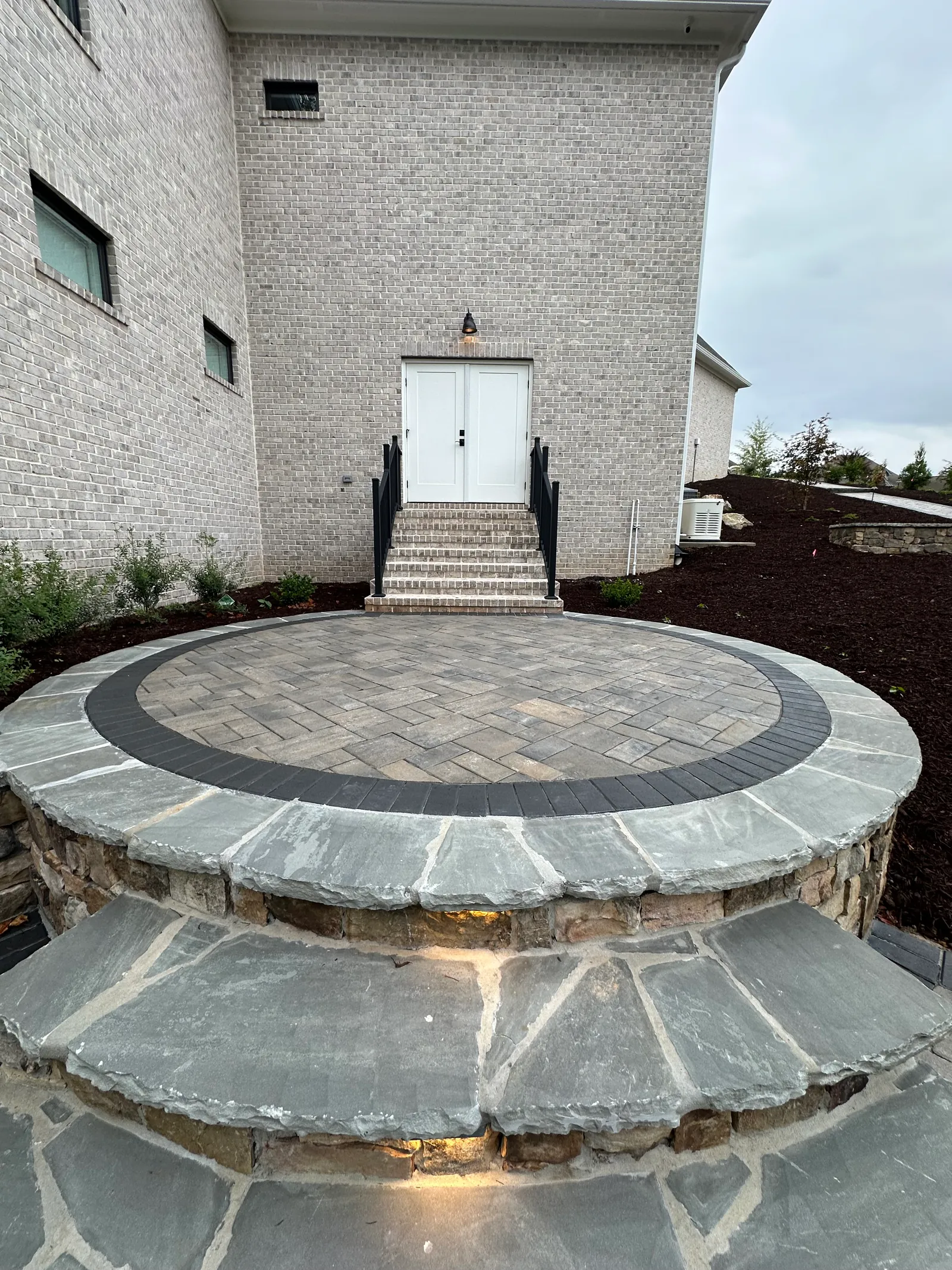 Curved stone steps and circular paver patio landing in front of a brick home, evening light