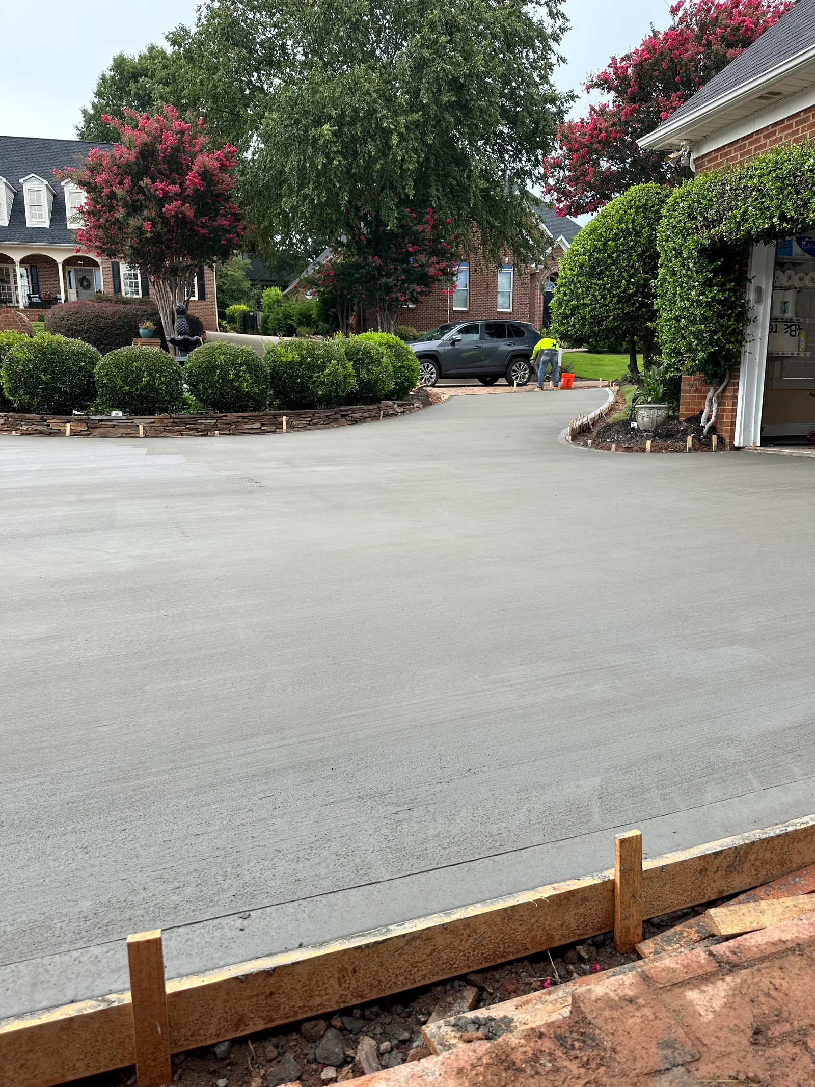 Freshly poured concrete driveway on a street lined with blooming crepe myrtle trees, brick homes on both sides