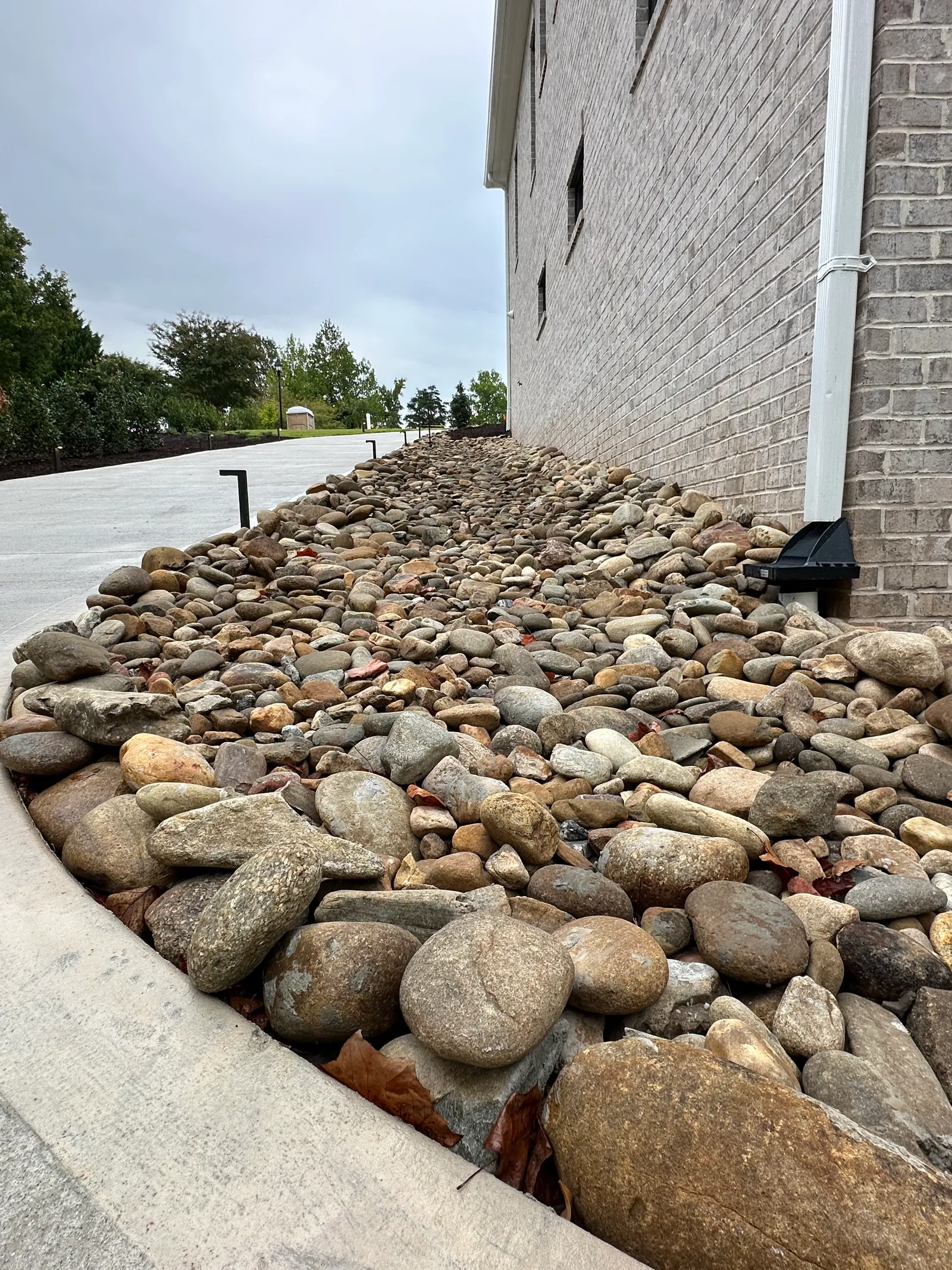 Close view of a river-rock drainage bed along a brick building foundation