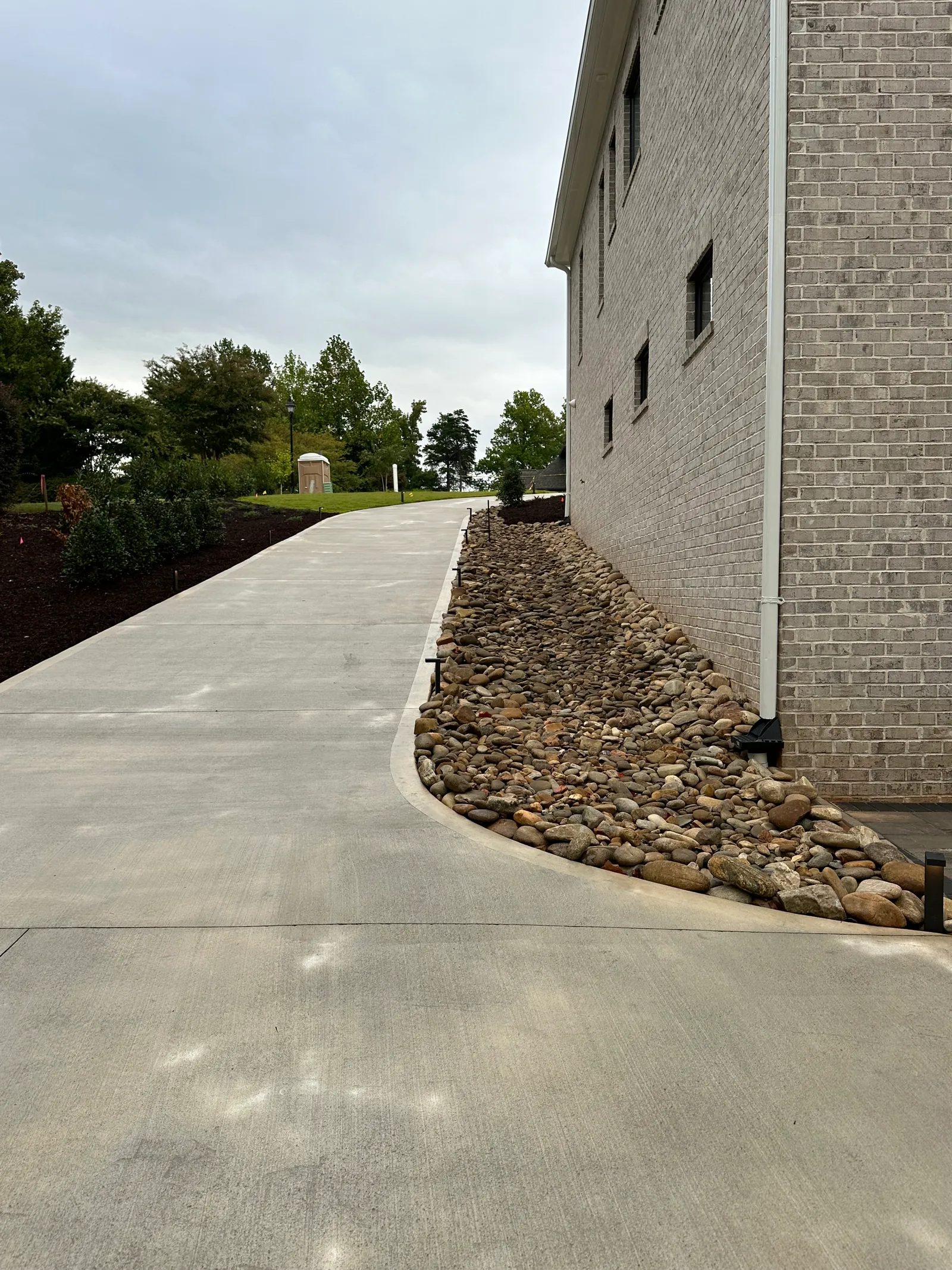 River-rock drainage bed running along a brick building foundation beside a concrete walkway
