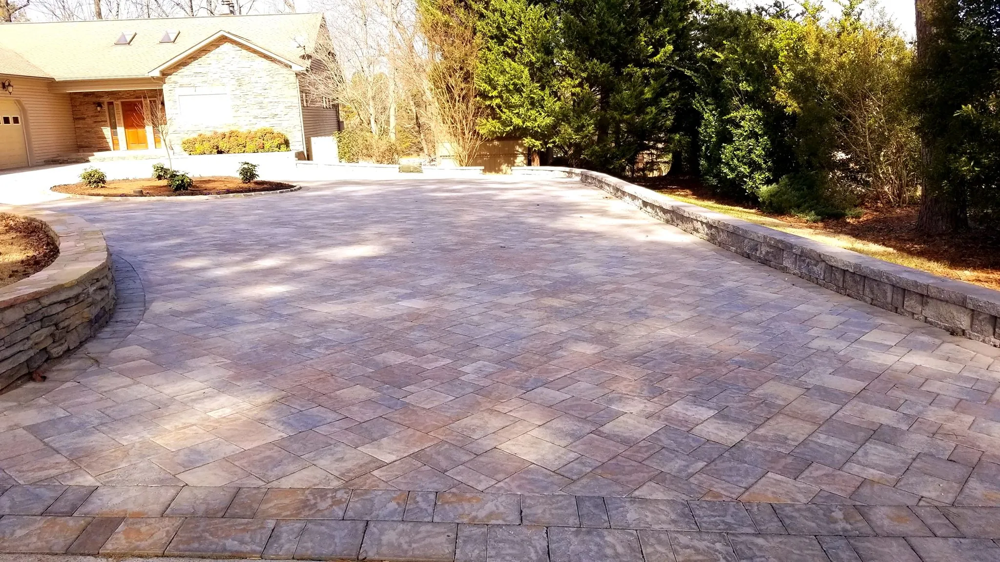 Circular paver motor court with a landscaped center island in front of a tan stone-and-siding home