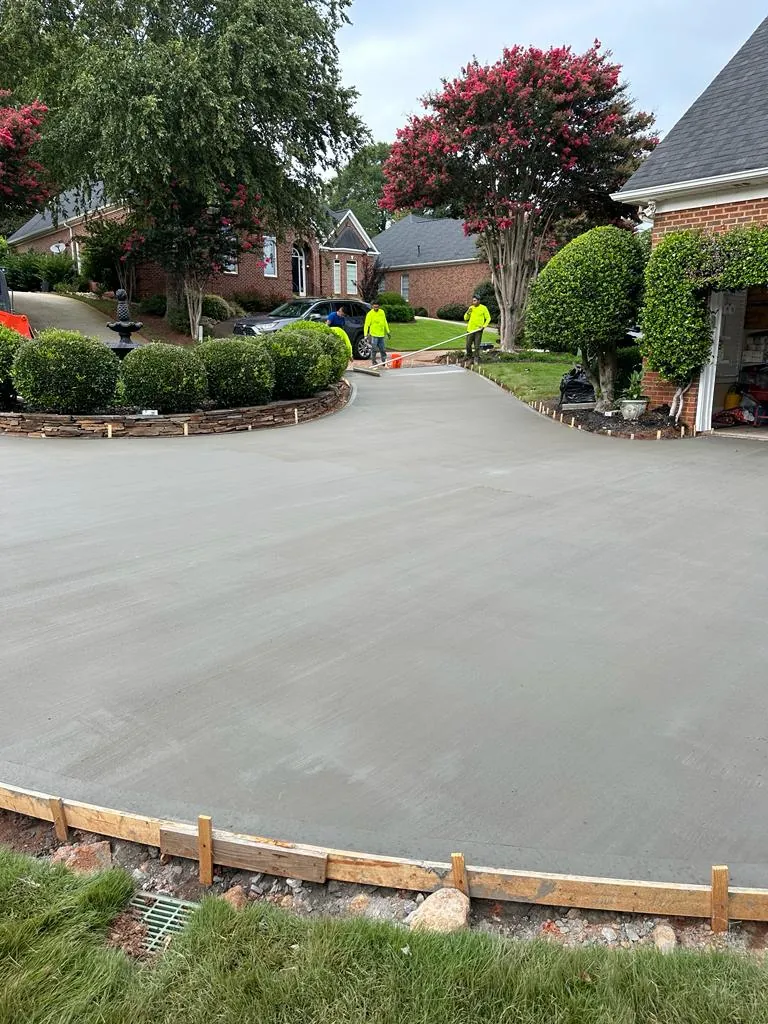 Crew finishing a poured concrete driveway, brick home, crepe myrtle trees in bloom