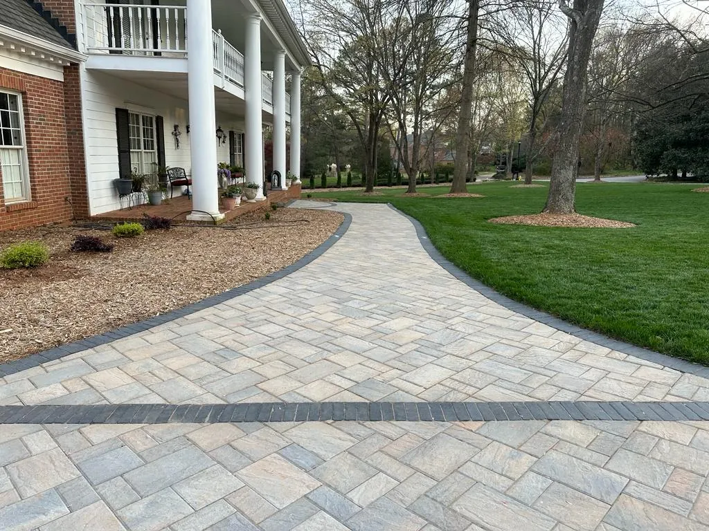 Paver motor court and walkway in front of a red brick two-story home with a white columned balcony