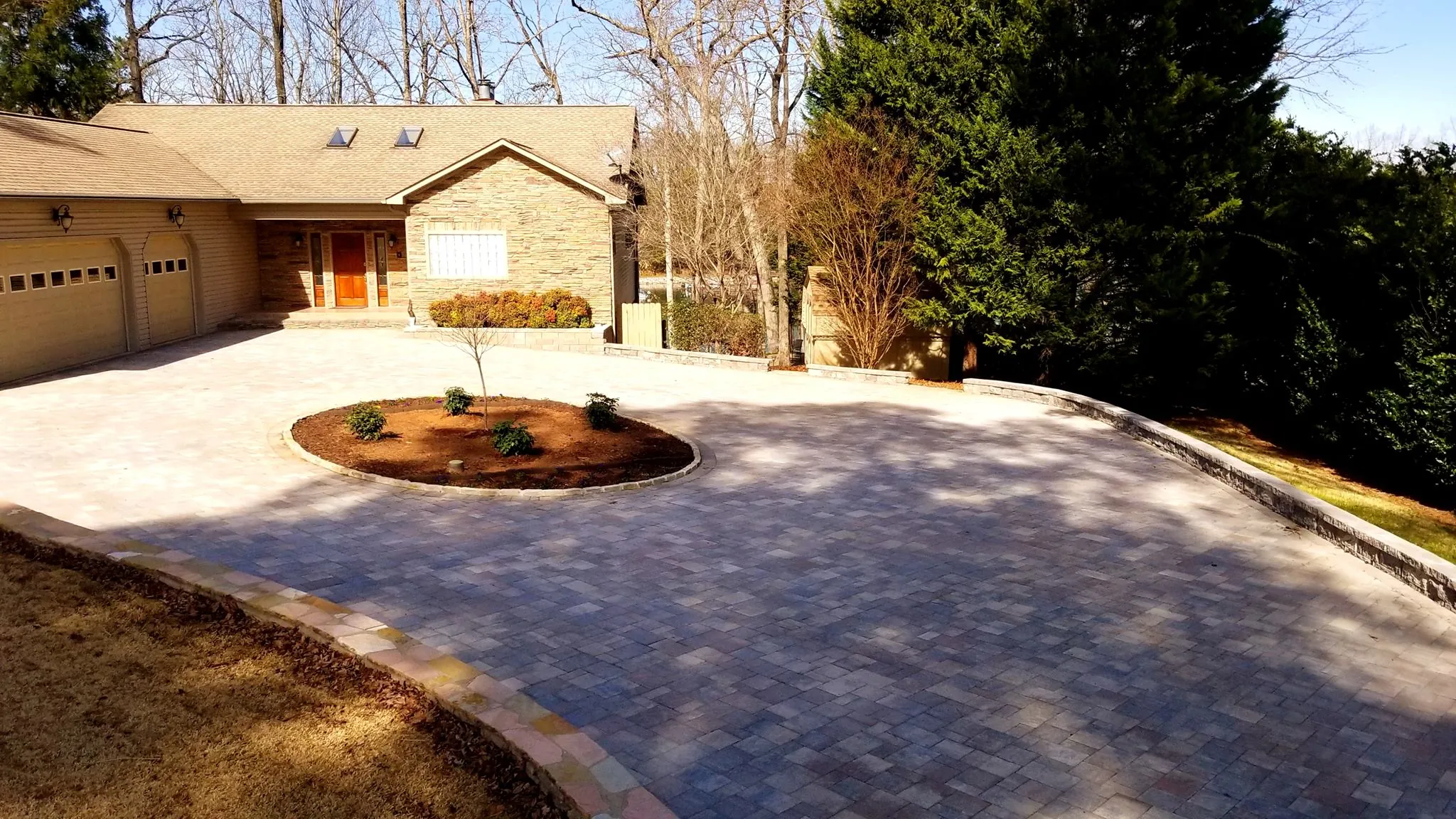 Tan stone home with a circular paver driveway and center planting island