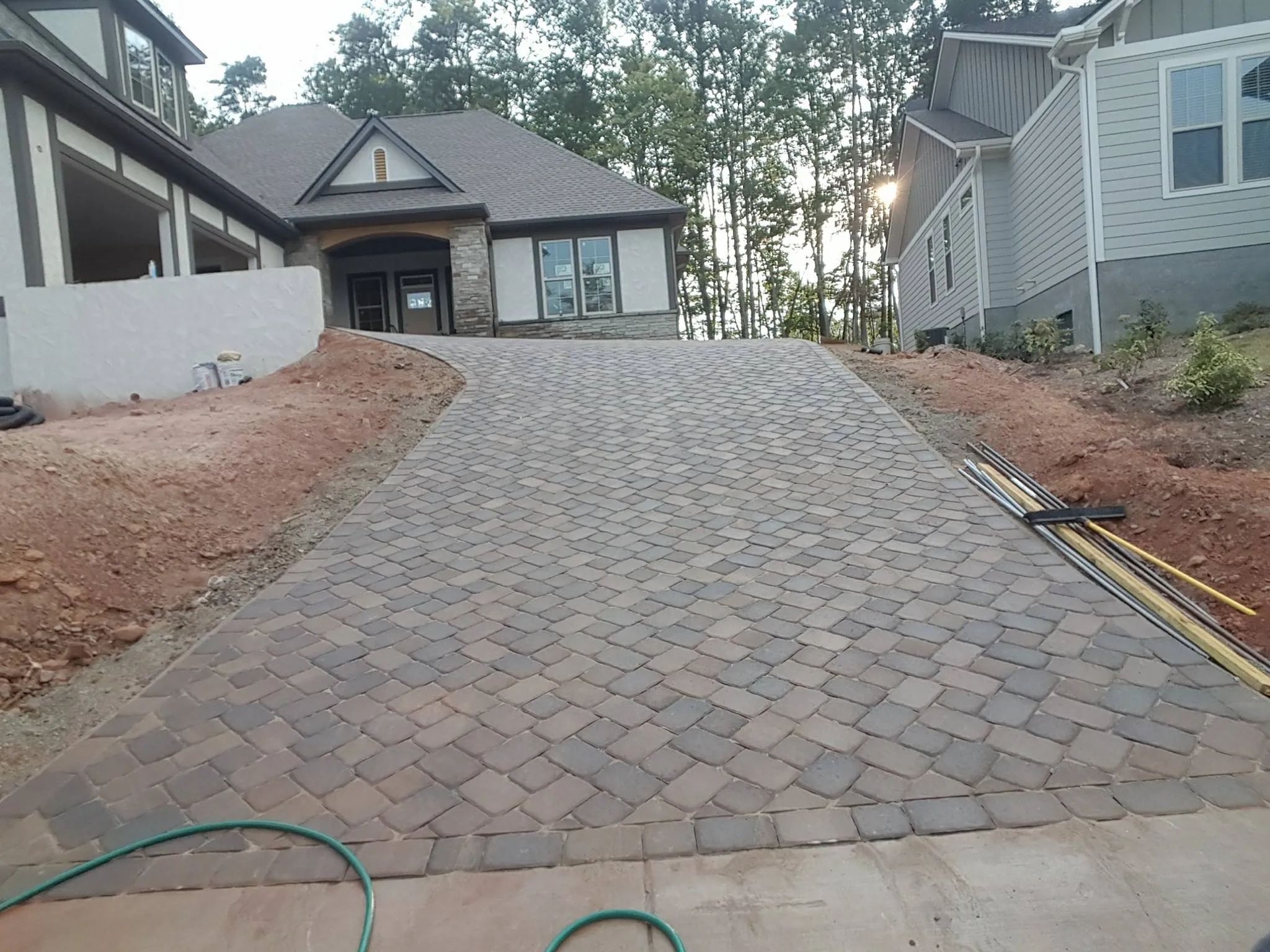Paver driveway under construction on a hillside lot, exposed red clay grading on both sides