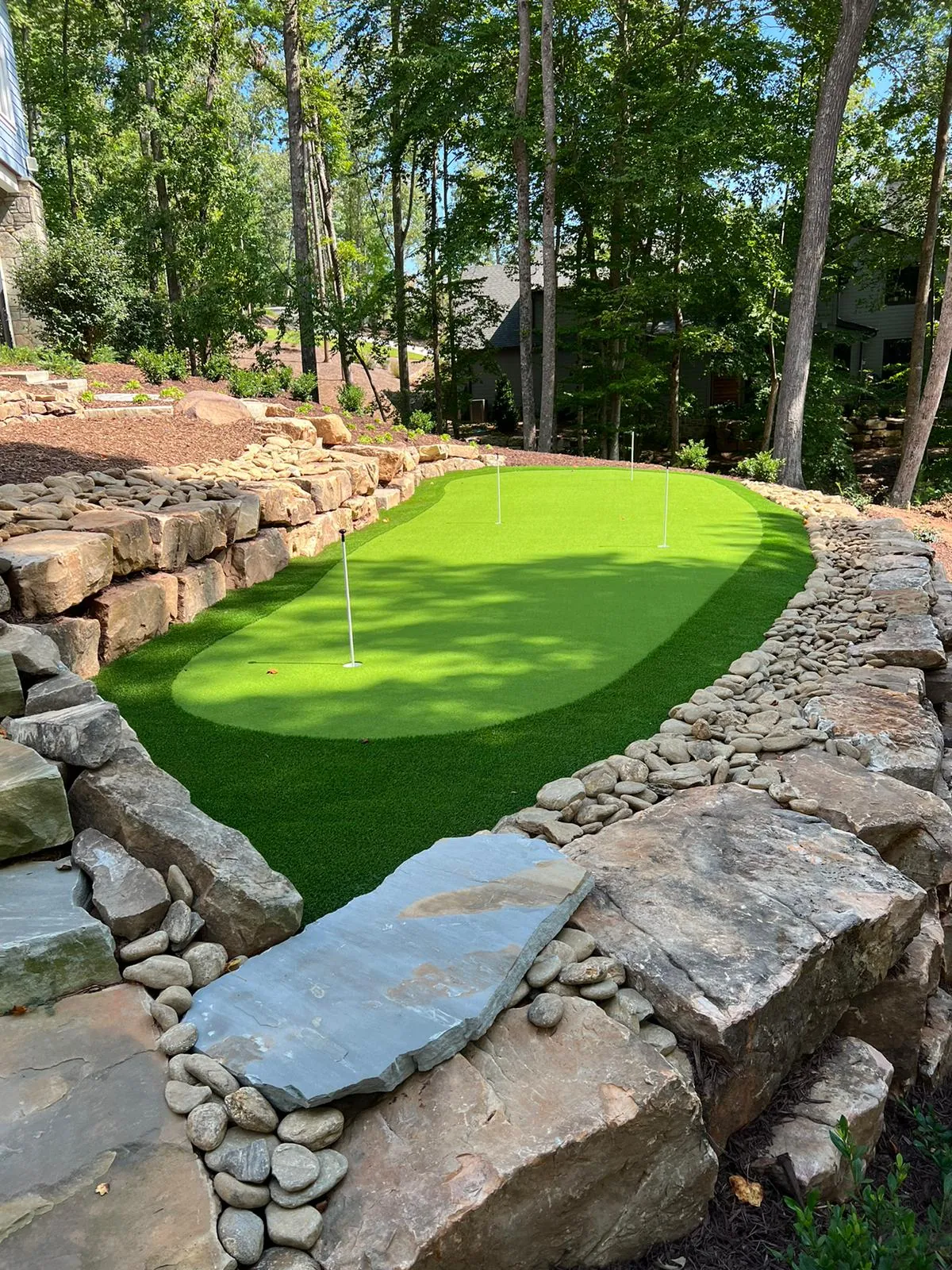 Artificial turf putting green terraced into a hillside with large natural boulder retaining walls