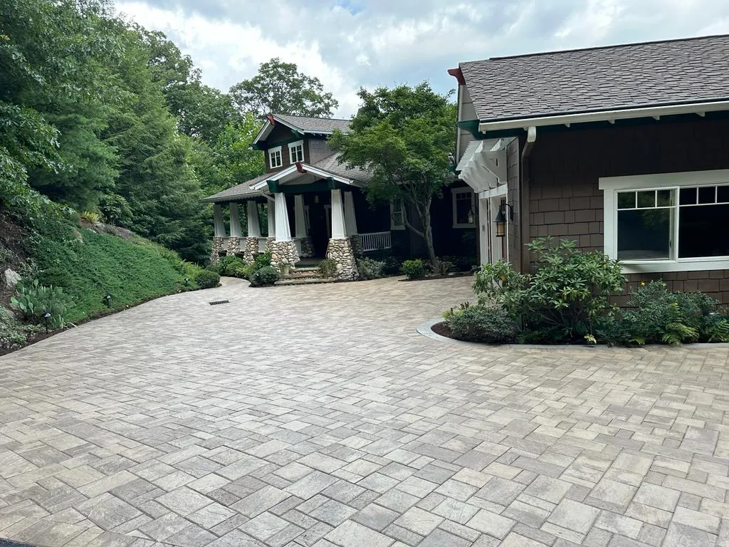 Paver motor court in front of a brown craftsman-style home with stone porch columns