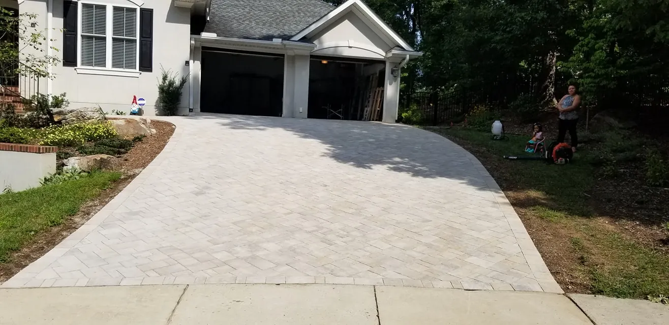 Herringbone-pattern paver driveway in front of a cream stucco home, family present