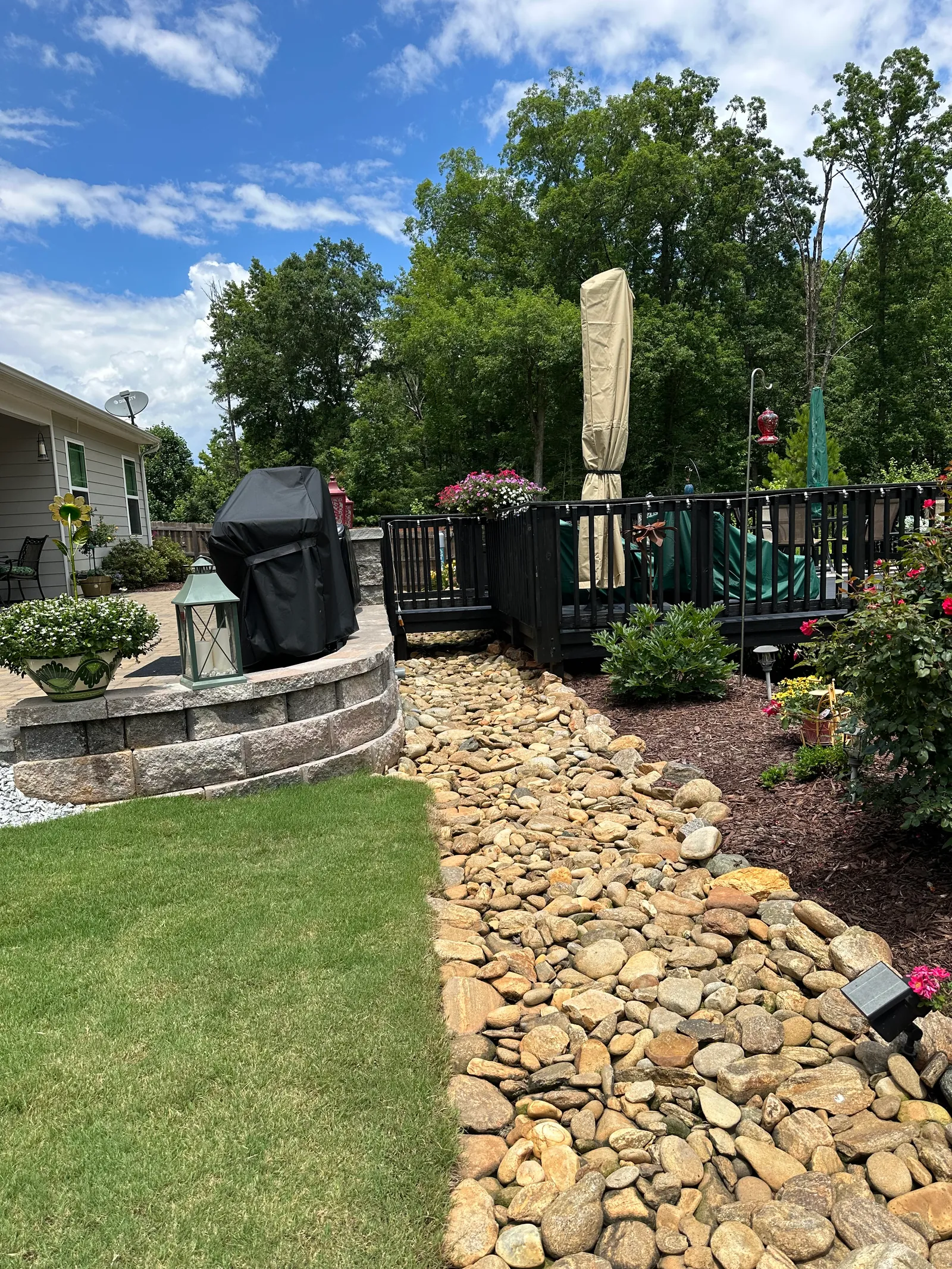River-rock drainage bed running past a stone seat wall toward a covered deck