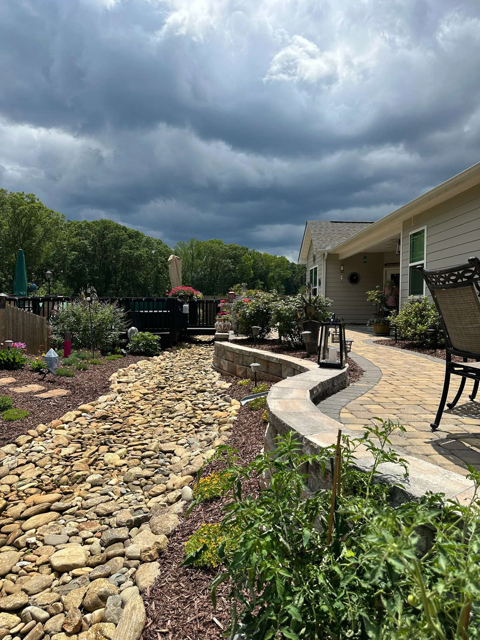 Curving river-rock dry creek drainage bed beside a stone-capped seat wall and paver walkway