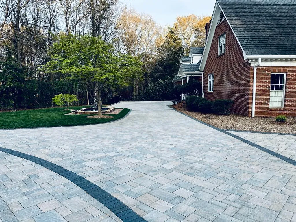 Paver driveway approach to a brick home with a fountain visible in the distance