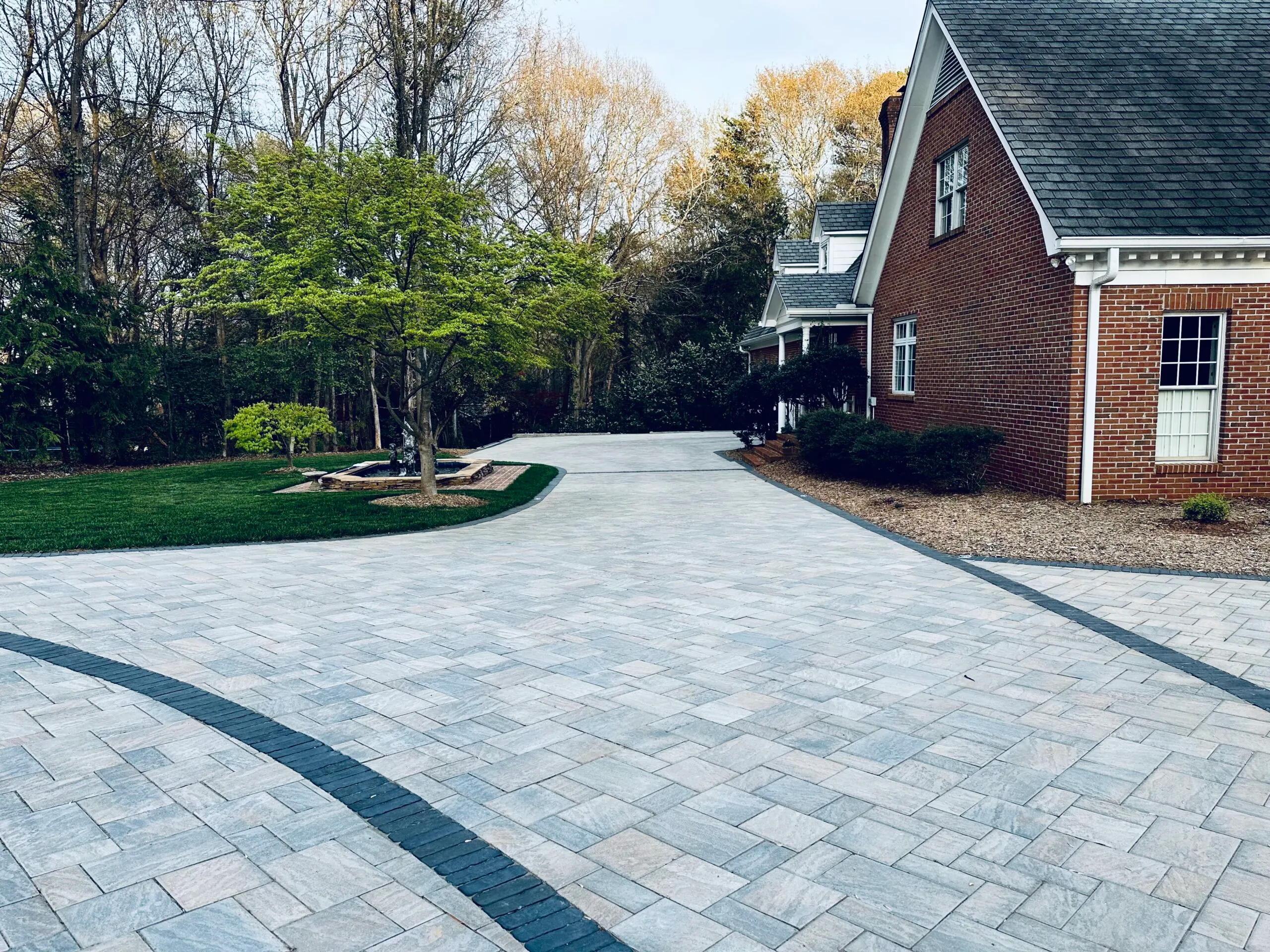 Large paver driveway with a contrasting dark border banding, curving toward a brick colonial home