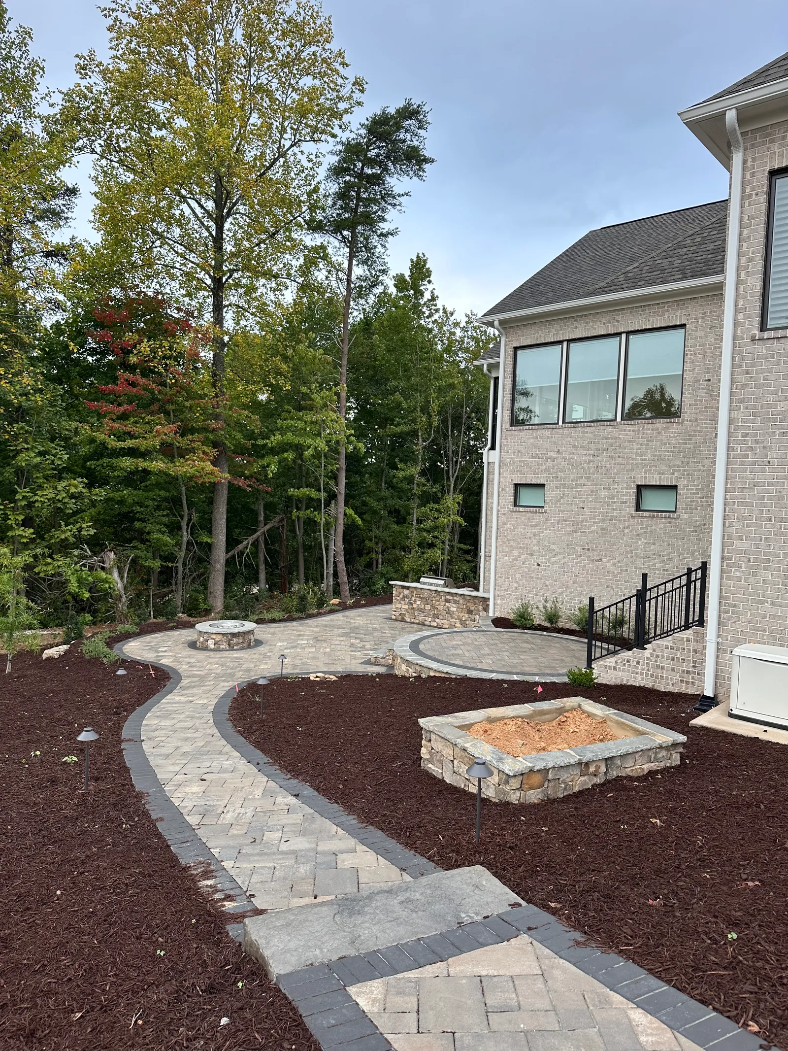 Round stone fire pit on a curving paver patio beside a stone-clad raised planter box