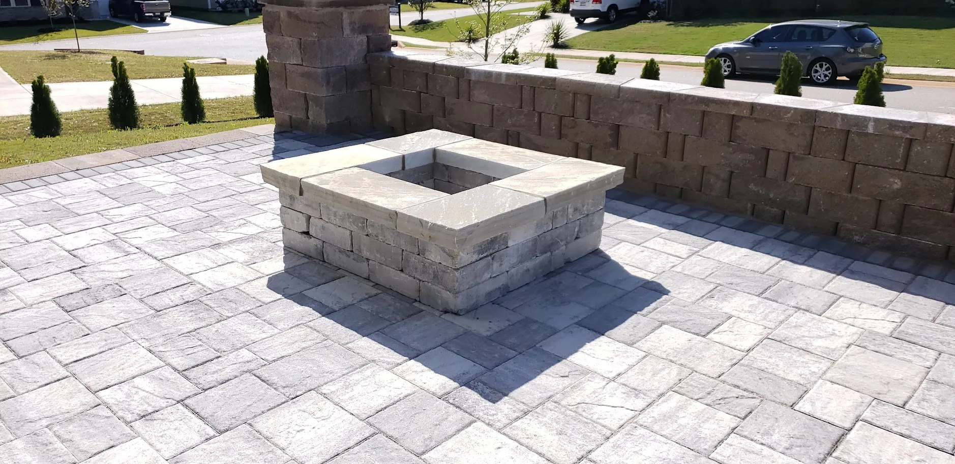 Square stone fire pit with a matching seat wall on a paver patio facing the street