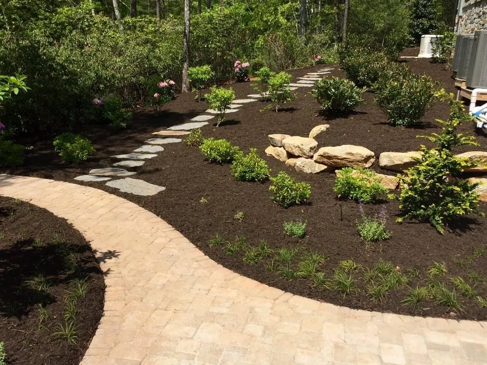Flagstone stepping-stone path through a freshly mulched planting bed with boulder accents