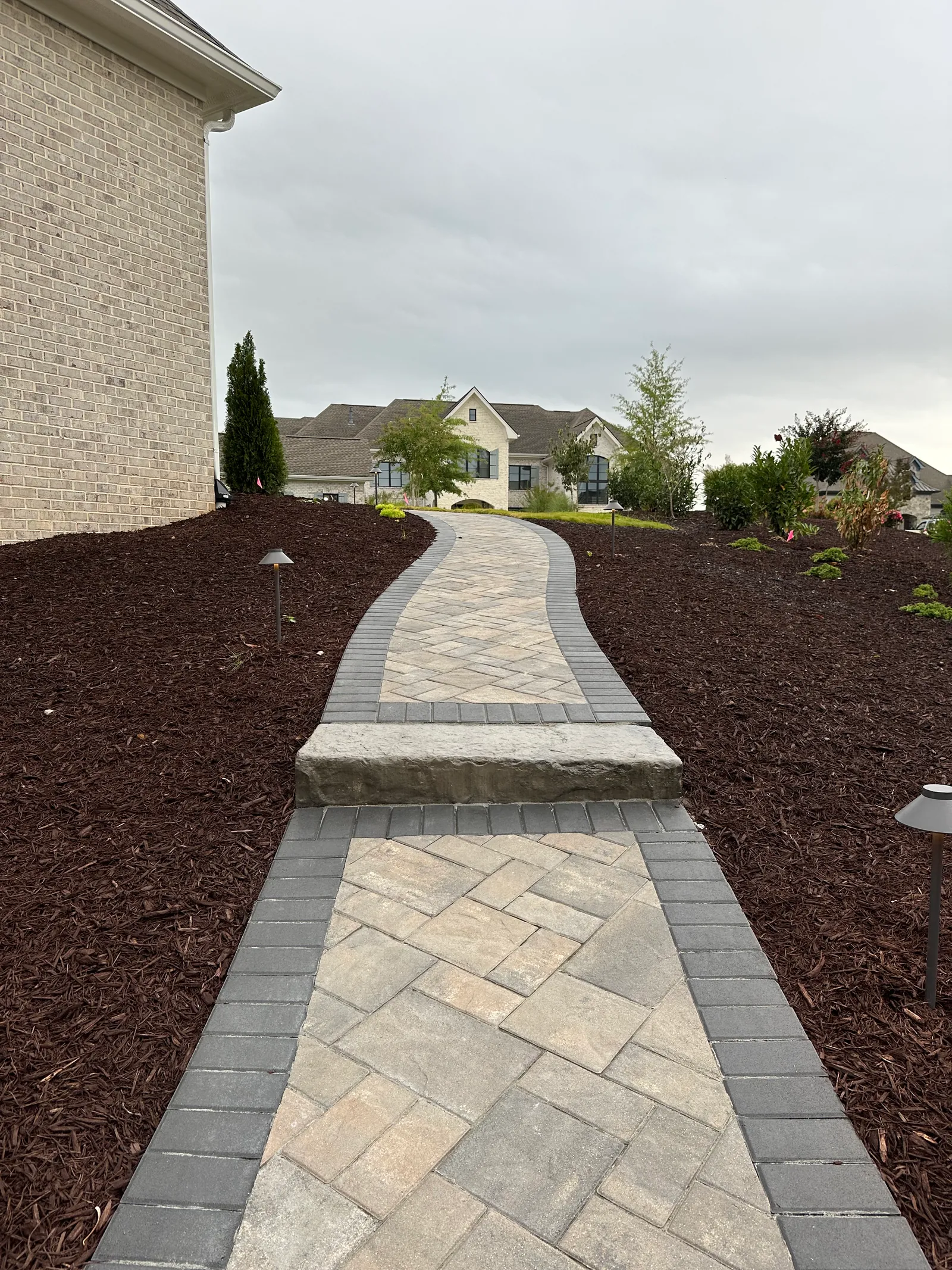 Herringbone-pattern paver walkway with a natural stone threshold step leading to a cream brick home