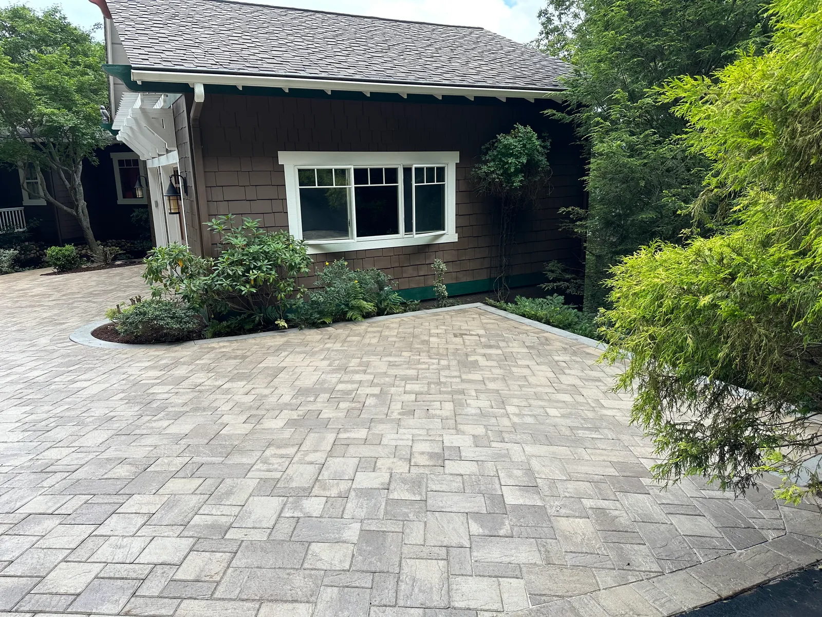 Paver motor court beside a craftsman-style home with dark shingle siding and a Japanese maple