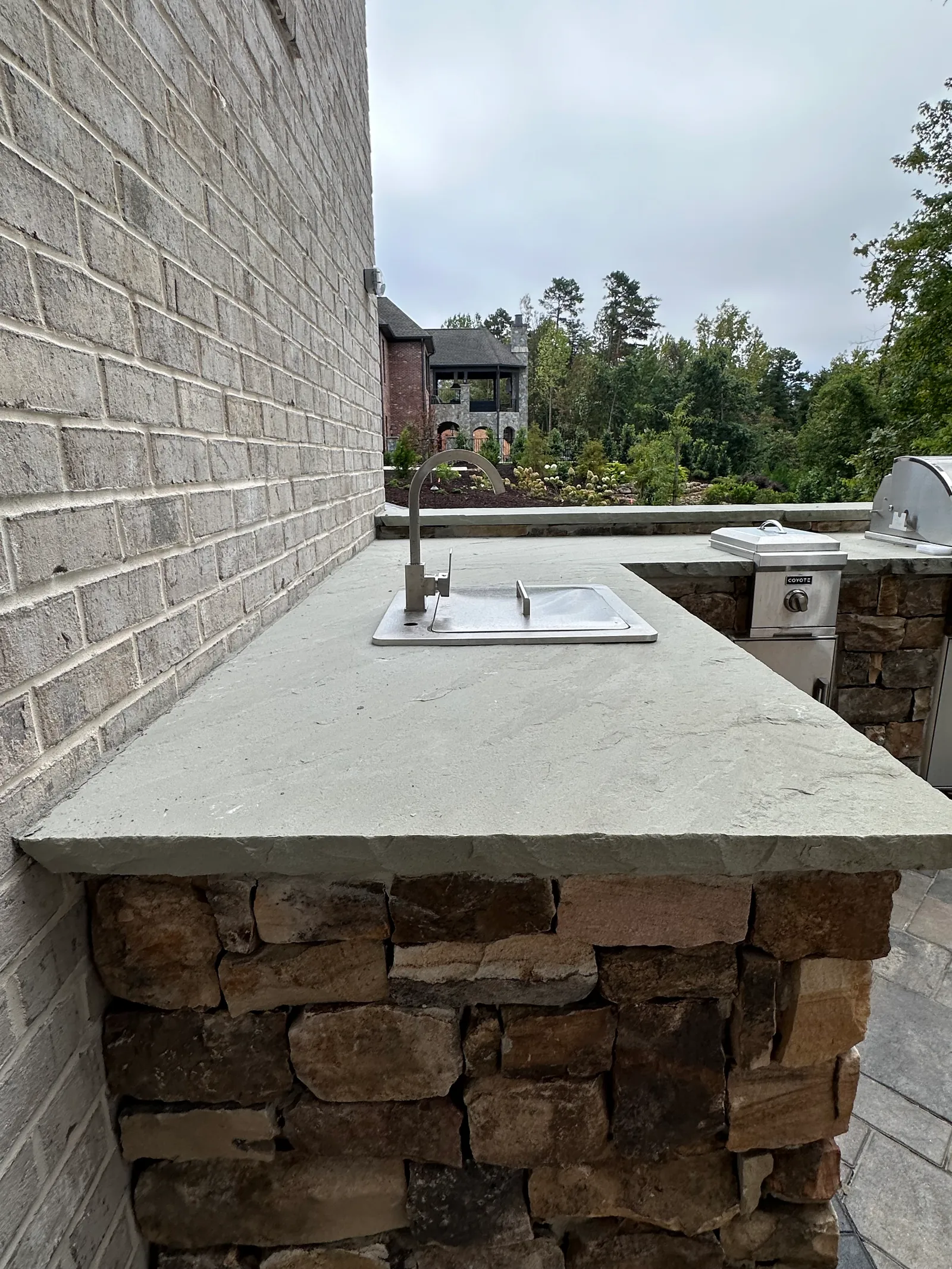 Outdoor kitchen countertop with a stainless sink and faucet, matching grill visible alongside