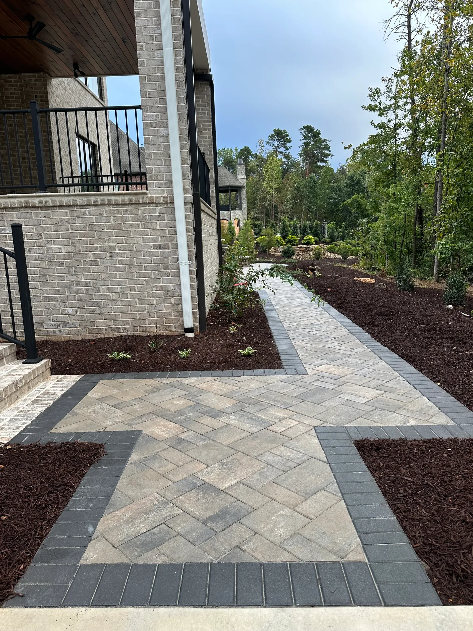 Herringbone paver walkway through a freshly mulched planting bed beside a stone building