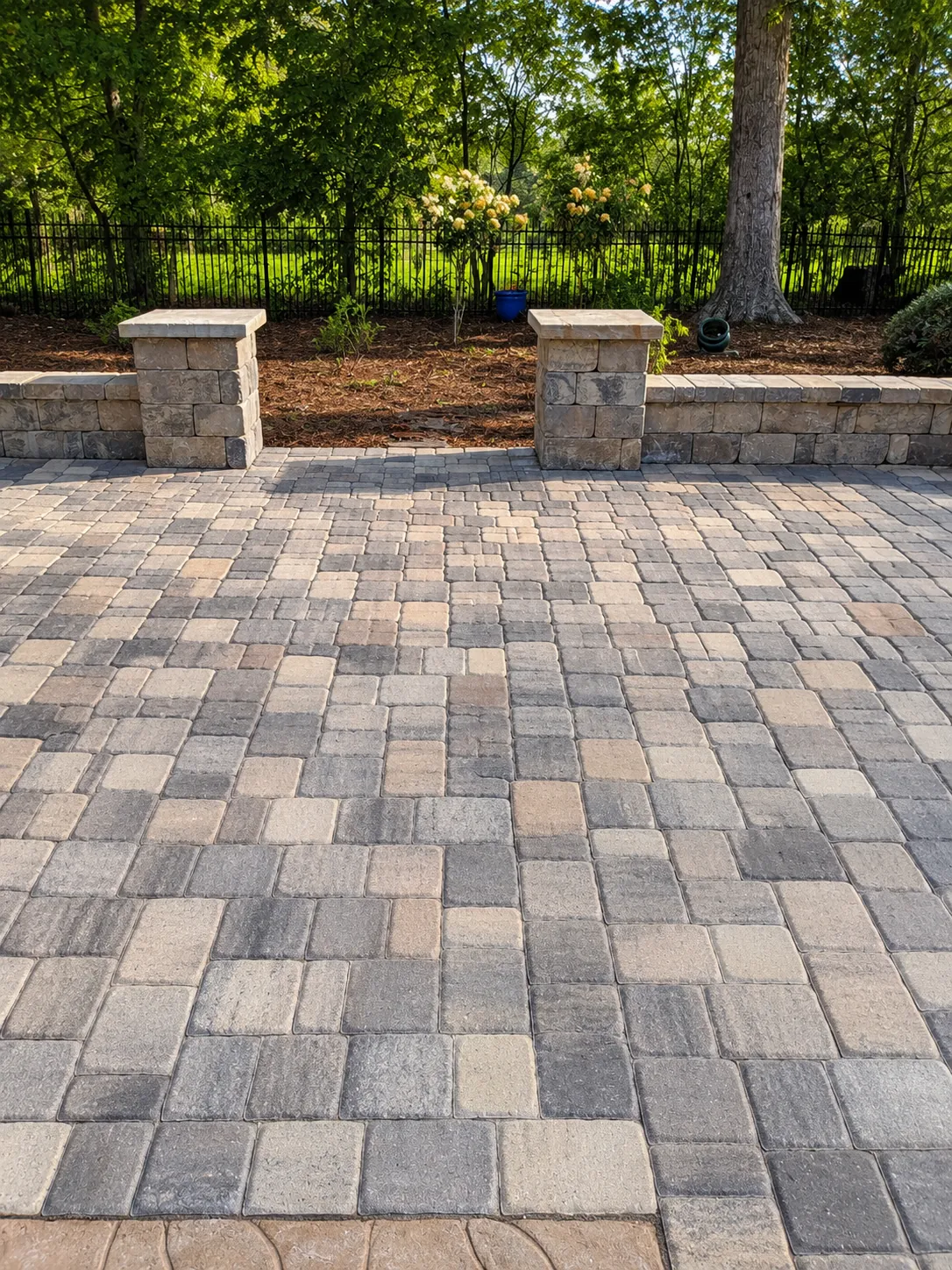 Multi-tone paver patio bordered by a low seat wall and stone-capped pillars beside flowering hydrangeas