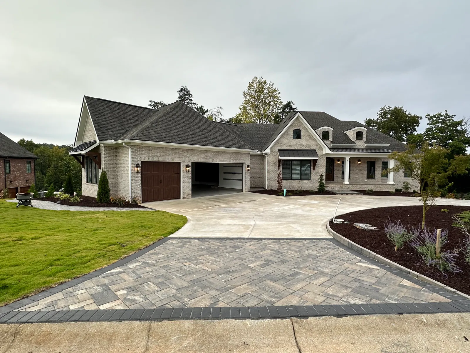 Paver-apron border on a concrete driveway in front of a large brick estate home with a three-car garage