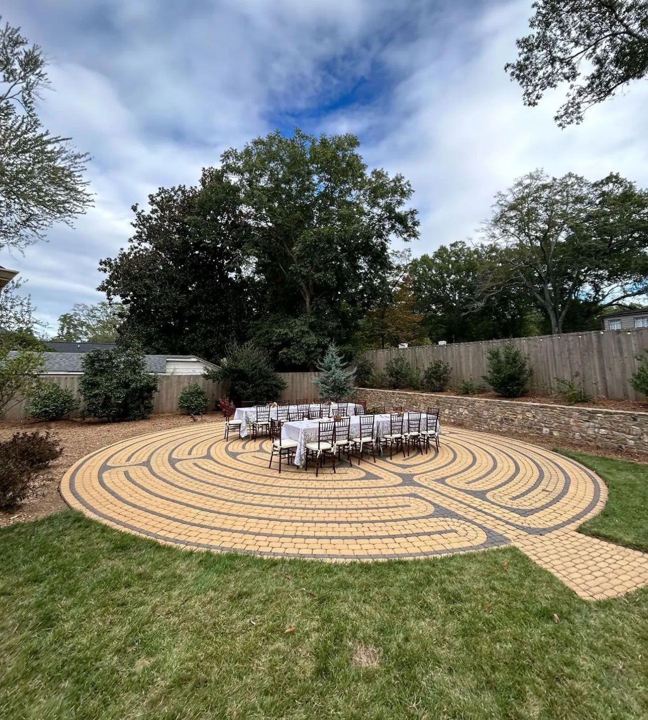 Circular paver walking labyrinth set in an open lawn bordered by a stacked-stone half-wall