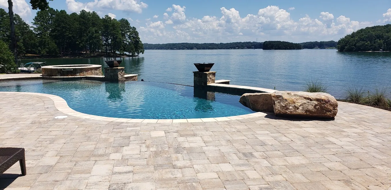 Infinity-edge pool with a natural stone paver deck and stone fire bowls, overlooking open water