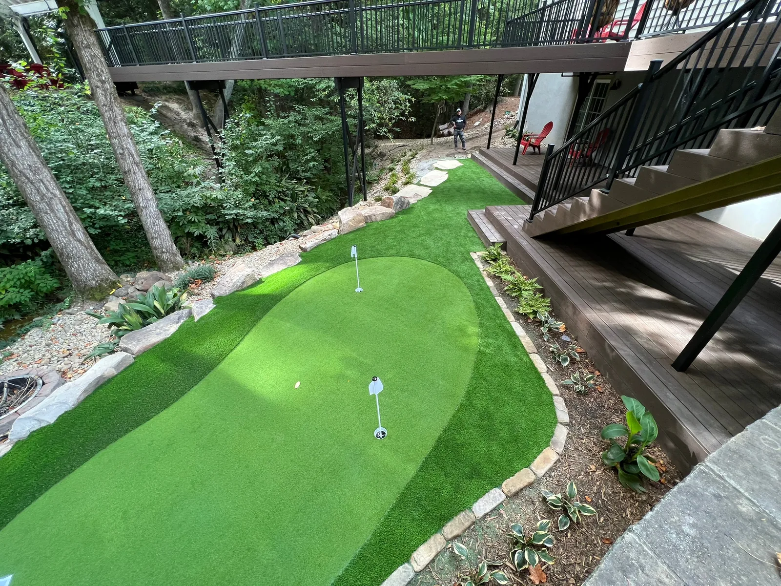 Narrow artificial turf putting green winding beneath an elevated deck on a wooded slope