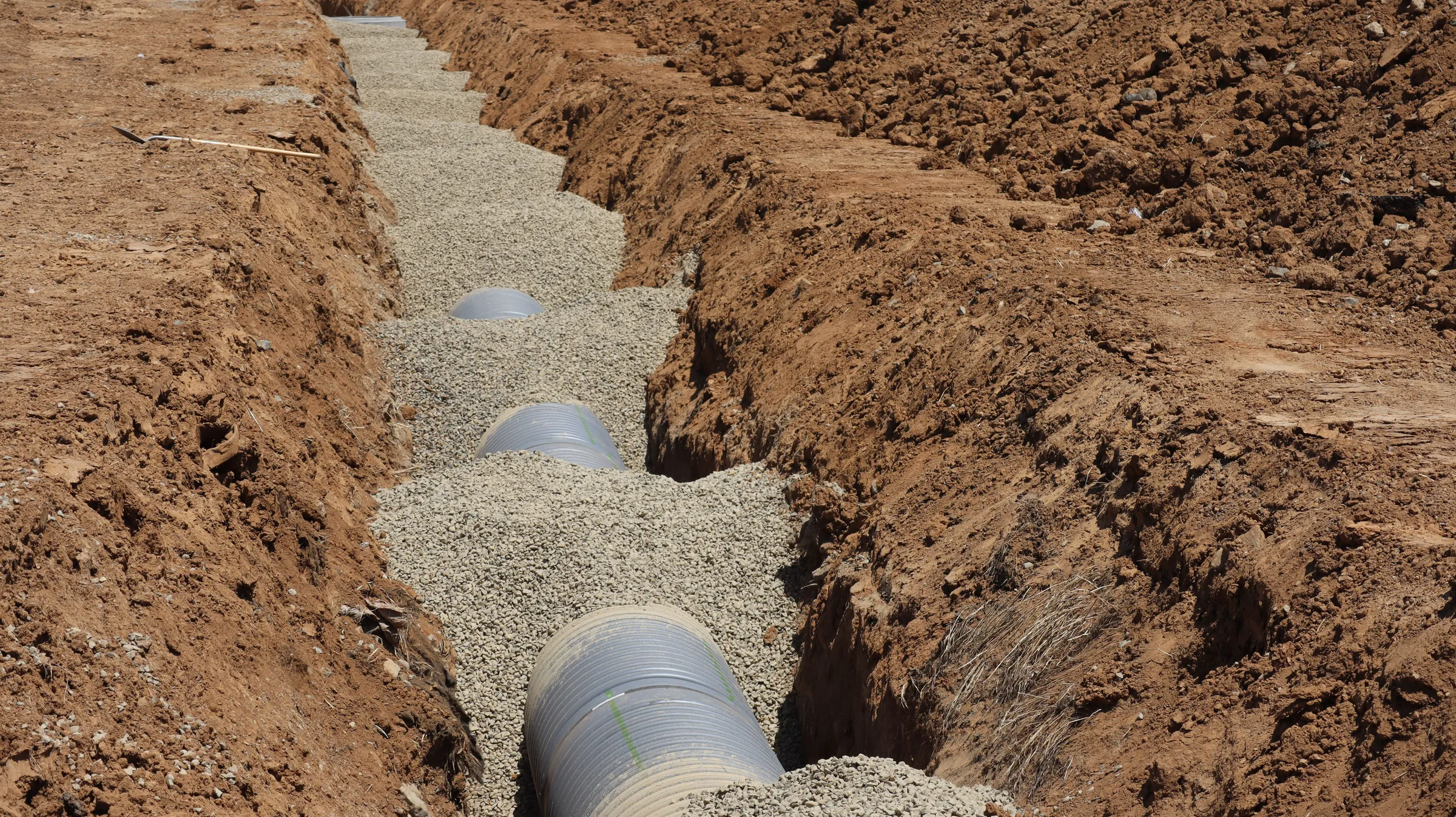 Corrugated drainage pipe being installed in a gravel-filled trench