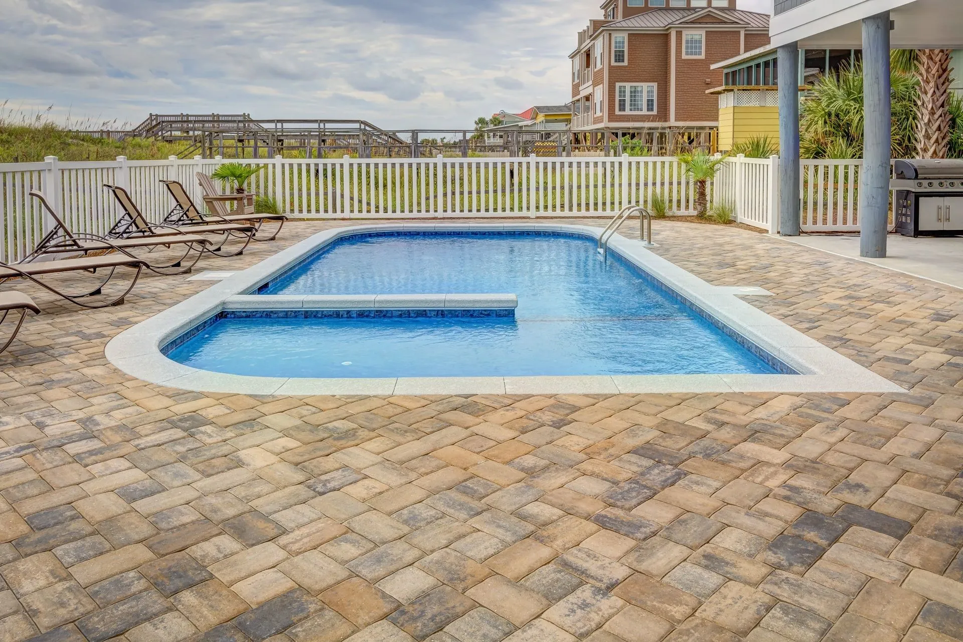 Paver pool deck surrounding a rectangular in-ground pool with lounge chairs