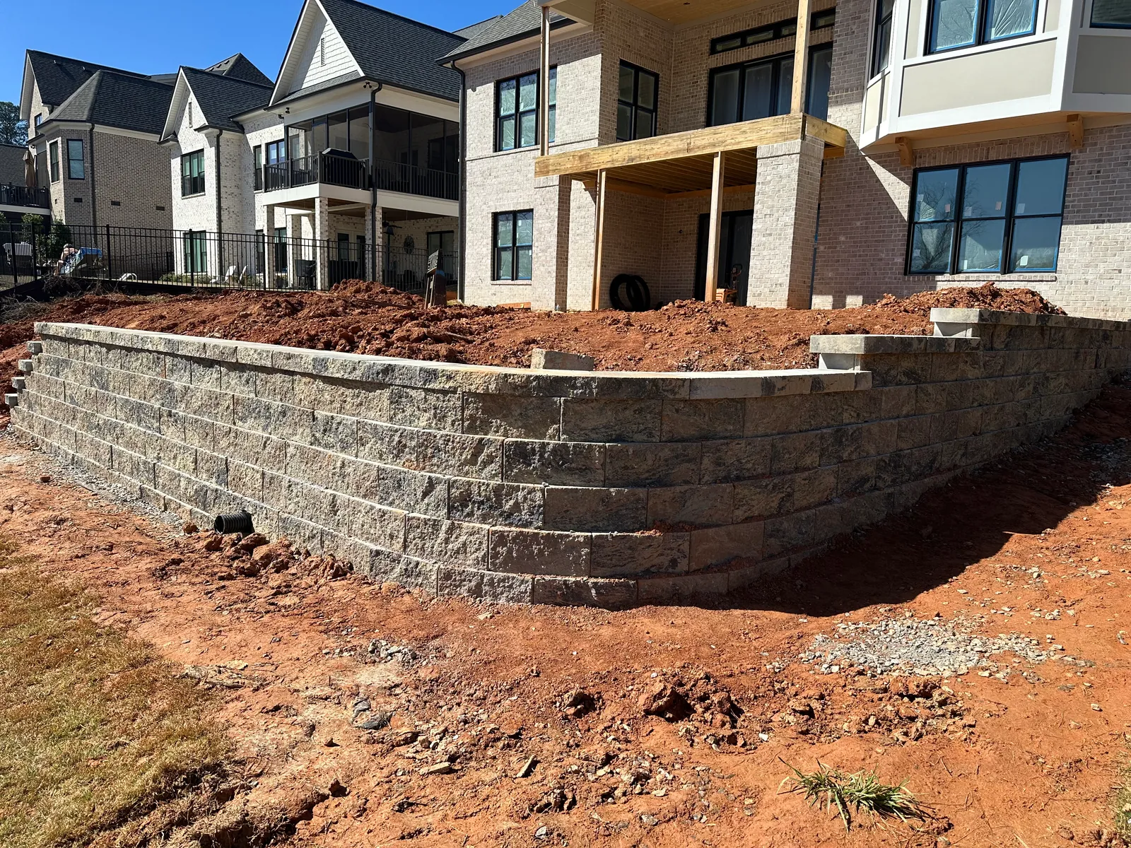 Curved segmental block retaining wall under construction beside a large brick home