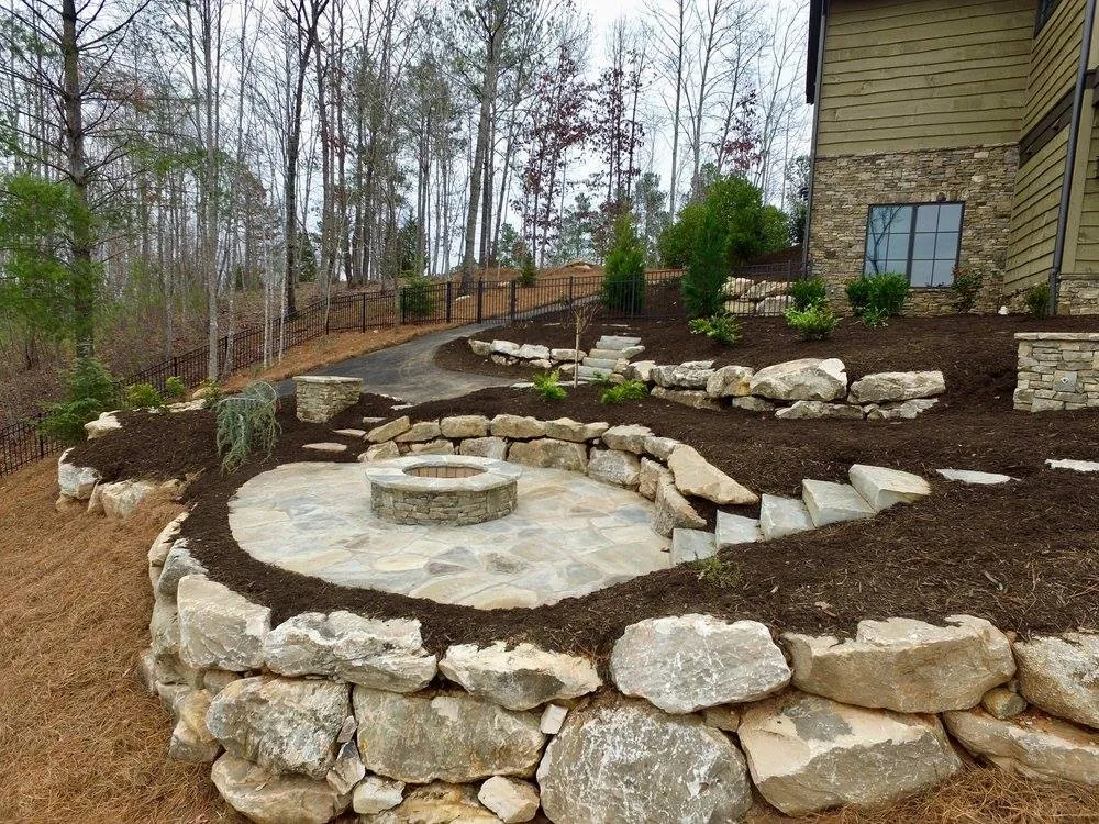 Flagstone fire pit patio built into a hillside with matching natural boulder retaining walls and stone steps