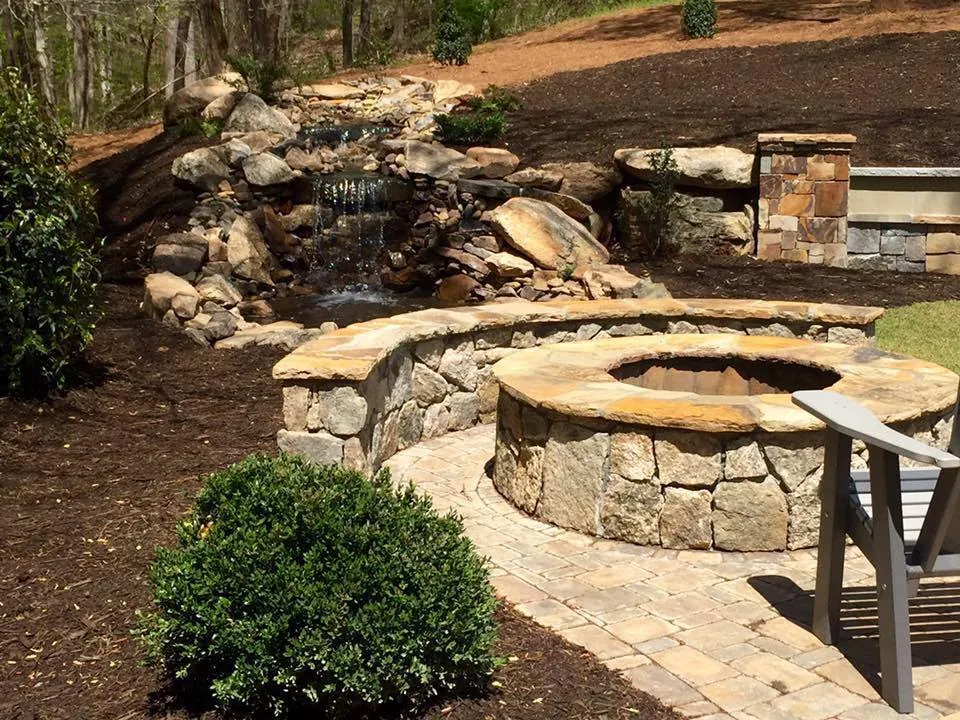 Closer view of a river-rock waterfall and pond feature beside a stone fire pit wall
