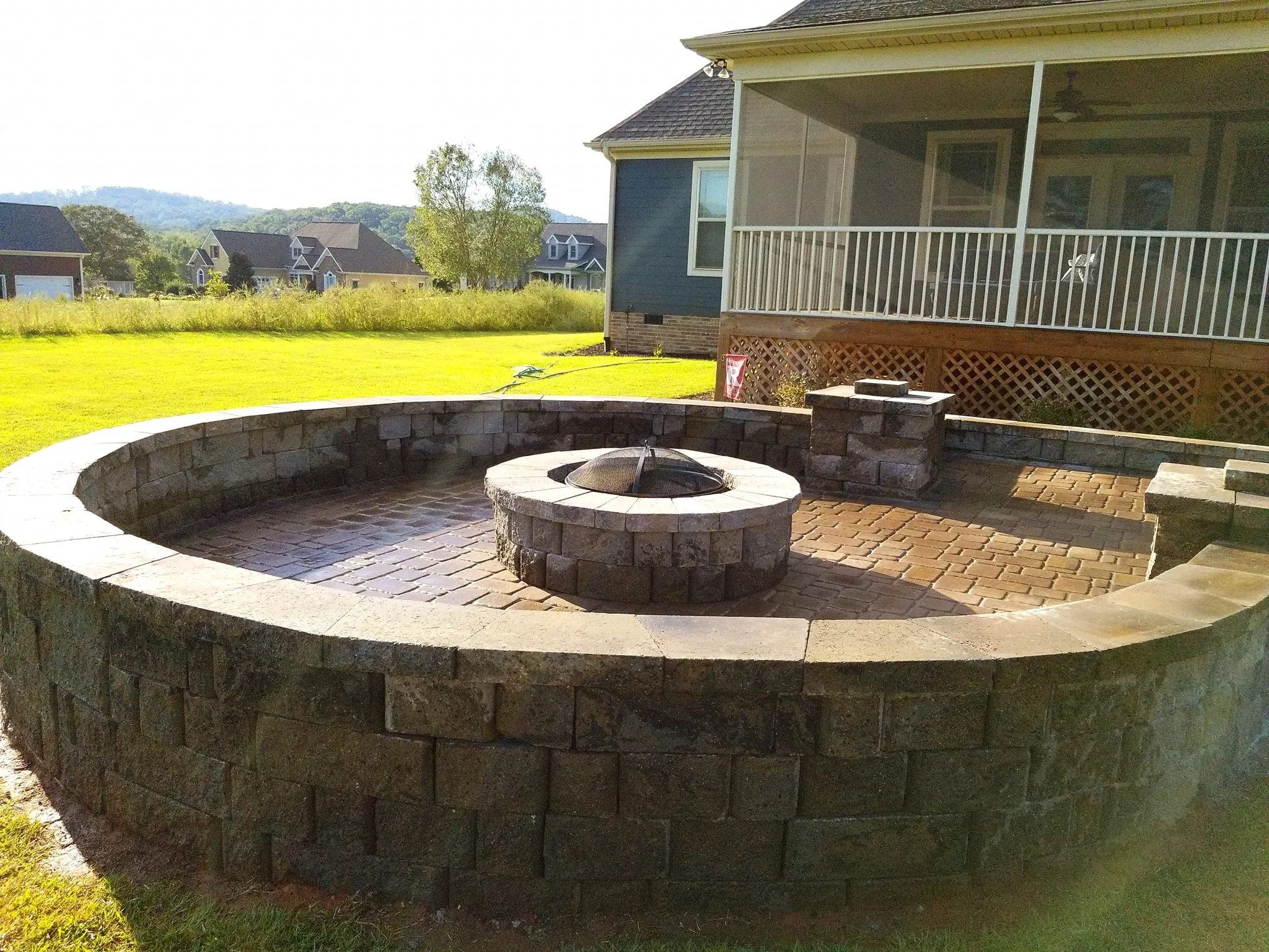 Circular paver patio with a built-in fire pit and curved seat wall, distant hills visible in the background