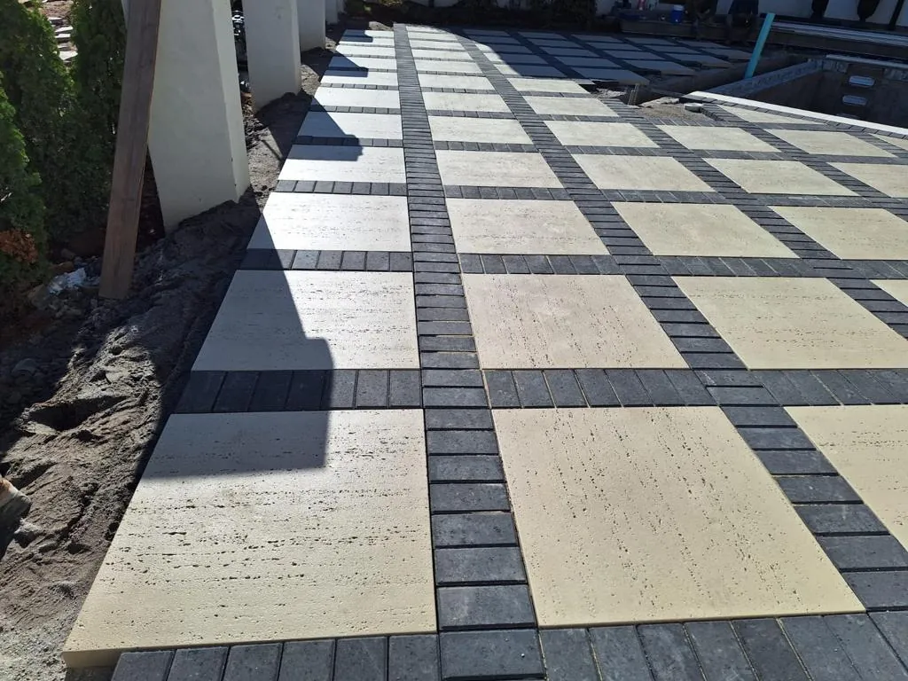 Pool deck under construction with a two-tone geometric paver pattern, pool visible under construction